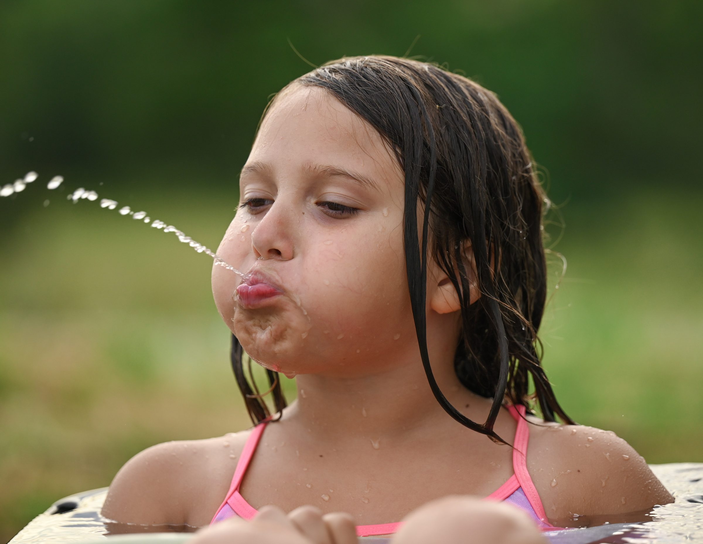 Child blowing a stream of water during a playful outdoor session